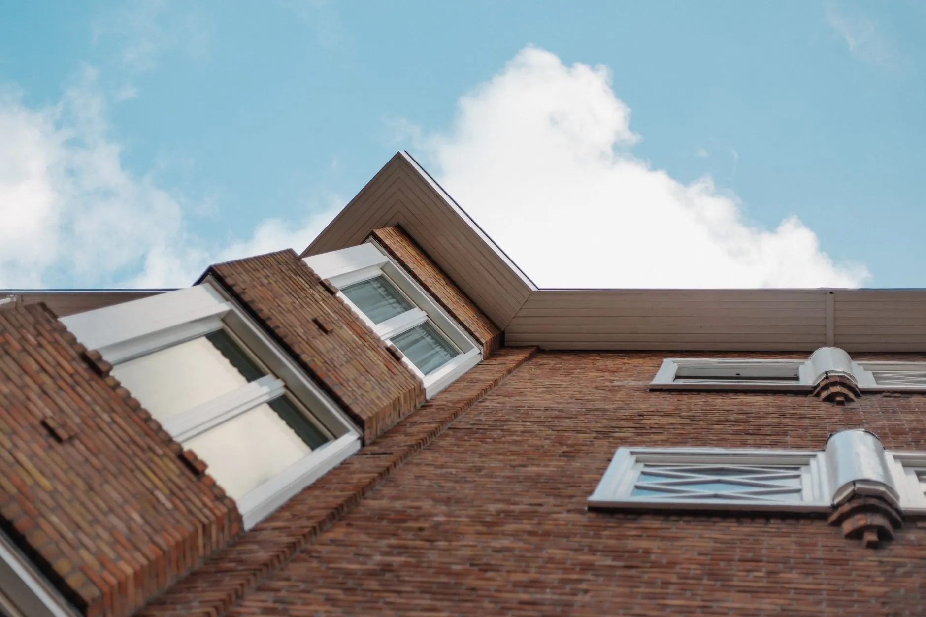 Brick roofline seen from below with white dormer windows and a new timber fascia against a blue sky.