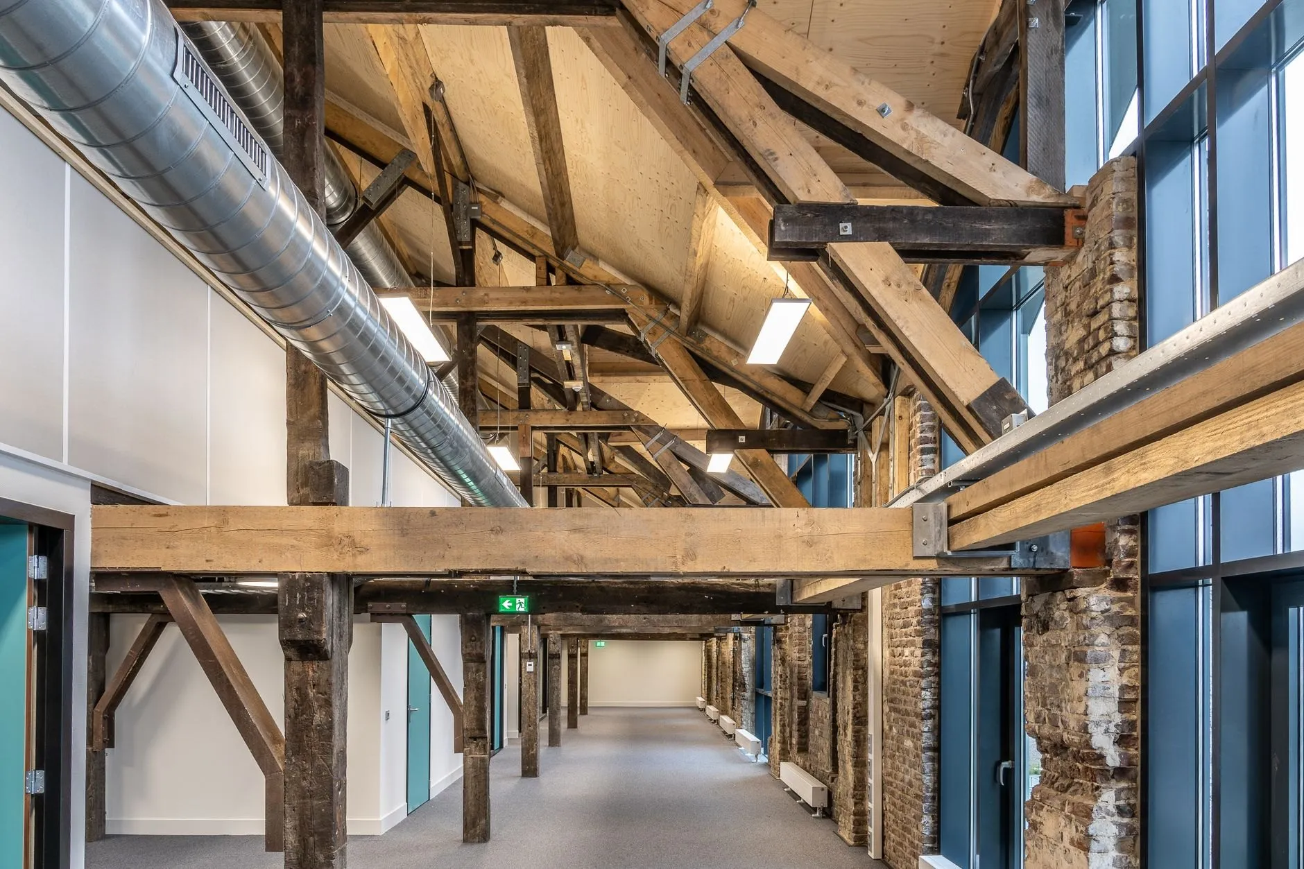 Studio floor under the original timber roof trusses, with a new beam, ductwork and exposed brick piers.