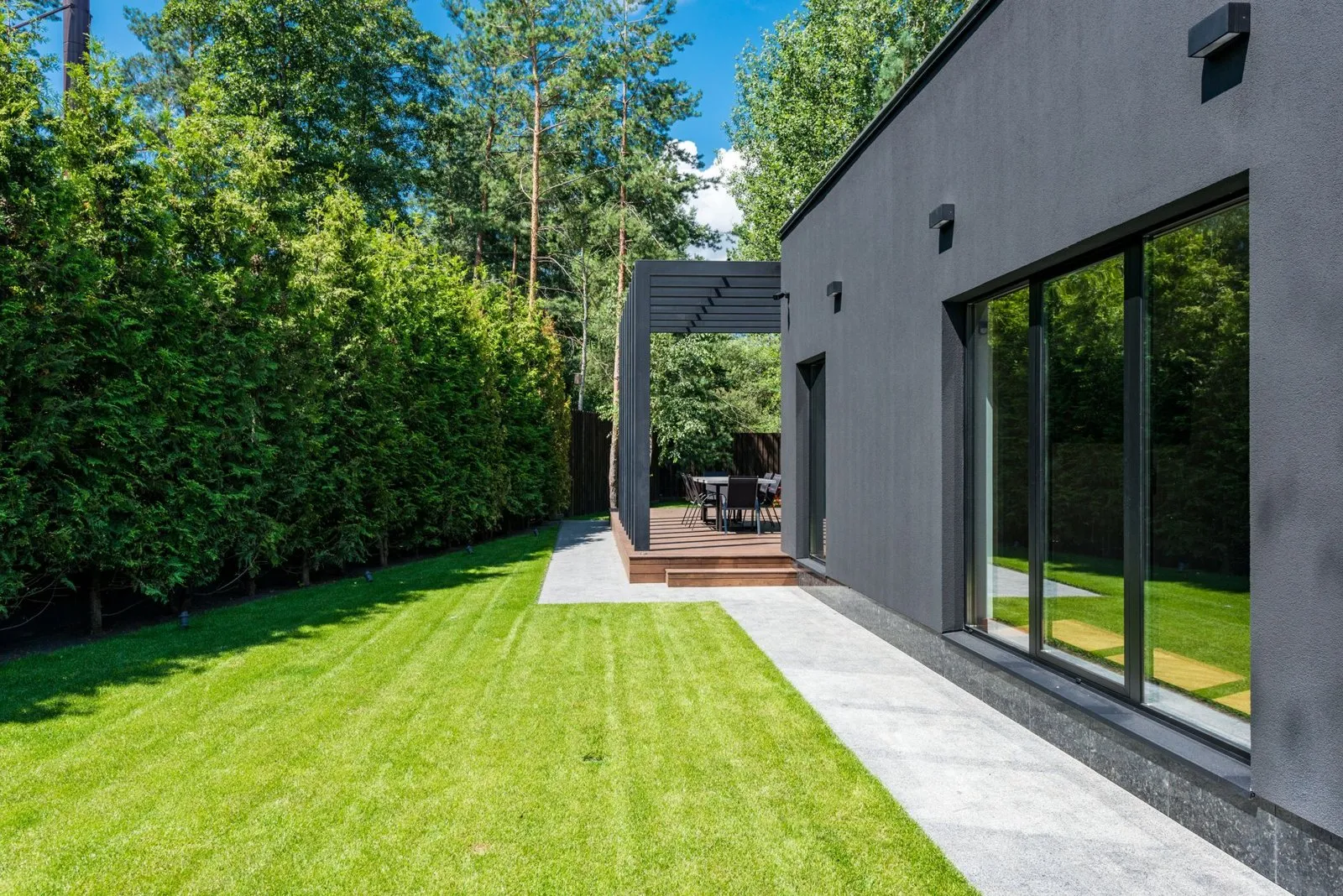 Side of the dark rendered mews house with a full-height sliding window and a stone path to the deck.